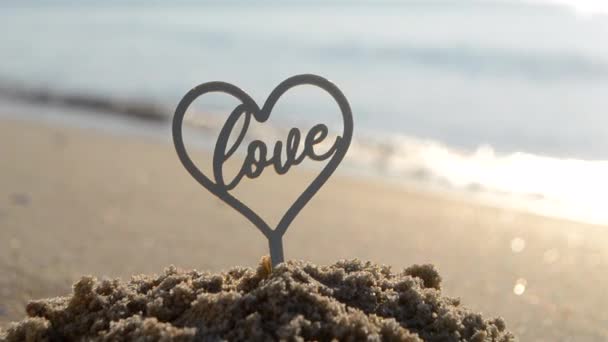 在阳光明媚的夏日里 沙滩上的爱在沙滩上的近照 在海浪的背景下 爱情是心形的 恋爱关系的浪漫概念 — 图库视频影像