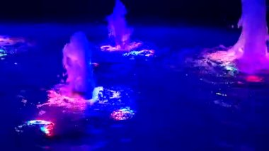 Geceleri renkli ışıklarla aydınlatılan sudaki çeşme. Yükselen ve çok renkli ışıkla aydınlatılan su akışı. Fıskiyeler fışkırıyor. Su basıncı, su kafa. Dekorasyon