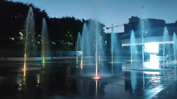 夜のカラフルなライトで照らされた歩行者地の噴水 市内の多彩な光に照らされた大きな公共の街の噴水 水のジェットが上昇して落ちる ウォータースプラッシュ — ストック動画