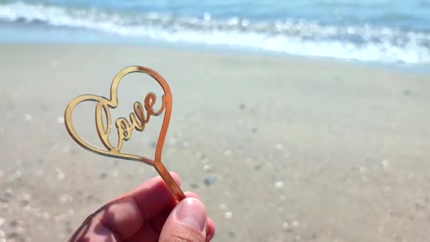 在阳光灿烂的夏日 人们手牵着手 形成了金子般的心形 爱情在背景沙滩上 海浪在海滨逼近 情人节 浪漫的爱情概念 — 图库视频影像