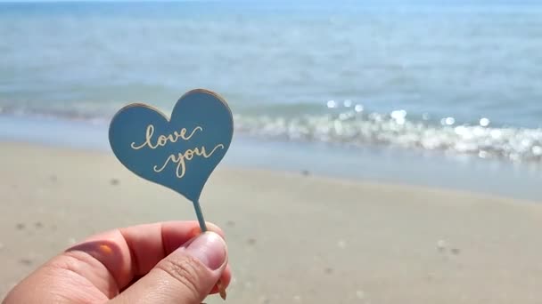 손가락에 플라스틱 모양의 심장과 단어를 해변과 해변에서 파도에 당신을 로맨스 — 비디오