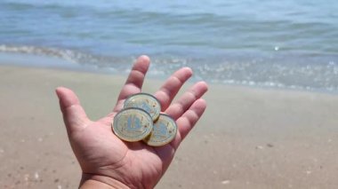 Bitcoin BTC sikkelerini elinde tutan adam güneşli bir günde kumlu sahilde arka plandaki deniz dalgaları üzerinde. Şifreli para kriptografi kripto para birimlerinin bitcoin 'lerini kavramsallaştır. Peer-to-peer ödeme ağı 3
