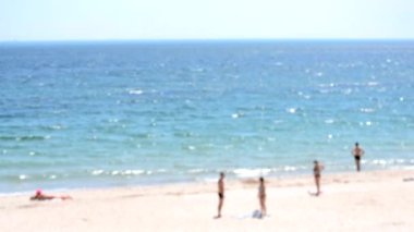 Birçok insan güneşli yaz günlerinde güneşli beyaz güneş lekeleriyle mavi deniz kıyısındaki kumlu sahilde ayakta, dinleniyor ve güneşleniyor. Deniz kıyısı ve deniz kıyısının soyut görüntüsü. Bulanık arkaplan