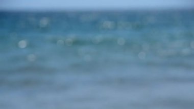 Bulanık arka plan mavi dalgalar beyaz köpükle deniz kıyısında yuvarlanıyor. Güneşin beyaz benekleri deniz dalgalarının üzerinde parlıyor. Deniz mavisi su. Sahil kıyısı Doğal arka plan Doğa