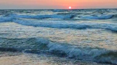 Fırtınalı deniz. Gün batımında ve şafakta denizde beyaz köpüklü büyük dalgalar. Mavi deniz, turuncu kırmızı gökyüzü ve güneş. Sahil kıyısı kıyı şeridi. Doğal arka plan doğa fırtınası