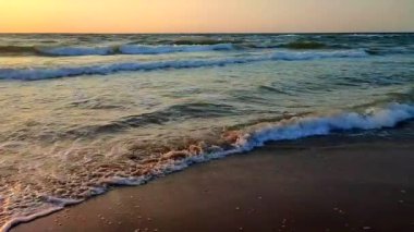 Fırtınalı deniz. Gün batımında ve şafakta denizde beyaz köpüklü büyük dalgalar. Mavi deniz, turuncu kırmızı gökyüzü. Kıyı sahili kıyı şeridi. Doğal zemin arkaplan fırtınası Yavaş çekim