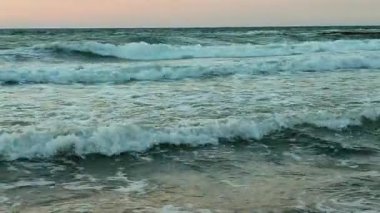 Fırtınalı deniz. Gün batımında ve şafakta denizde beyaz köpüklü büyük dalgalar. Mavi deniz, turuncu kırmızı gökyüzü. Kıyı sahili kıyı şeridi. Doğal arka plan doğa fırtınası