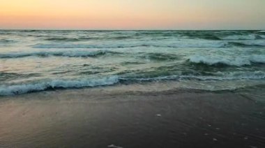 Fırtınalı deniz. Gün batımında ve şafakta denizde beyaz köpüklü büyük dalgalar. Mavi deniz, turuncu kırmızı gökyüzü. Kıyı sahili kıyı şeridi. Doğal zemin arkaplan fırtınası Yavaş çekim