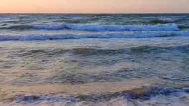 Fırtınalı deniz. Gün batımında ve şafakta denizde beyaz köpüklü büyük dalgalar. Mavi deniz, turuncu kırmızı gökyüzü. Kıyı sahili kıyı şeridi. Doğal zemin arkaplan fırtınası Yavaş çekim