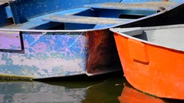 Güneşli bir günde mavi ve turuncu renkli eski tekneler suda. Eski püskü püskü botlar, nehrin sakin sularında rıhtımın yakınındaki küçük tekneleri tırmaladı. Turizm turizmi, yolculuk, ulaşım, dinlenme.