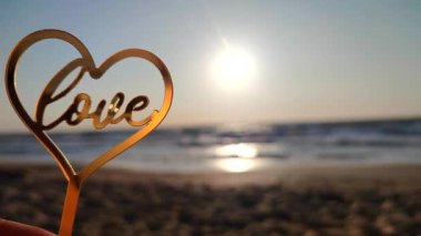 Elinde kalp şeklinde sarı yansıtıcı çubuk tutan kadın ve güneşli bir sabahta kumlu sahil sahilinde parlayan güneşin arka planında aşk kelimesi. Romantik Sevgililer Günü 'nü severim.