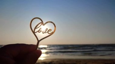 Elinde kalp şeklinde sarı yansıtıcı çubuk tutan kadın ve güneşli bir sabahta kumlu sahil sahilinde parlayan güneşin arka planında aşk kelimesi. Romantik Sevgililer Günü 'nü severim.