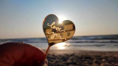 Elinde kalp şeklinde sarı yansıtıcı çubuk tutan kadın güneşli bir sabahta kumlu sahil sahilinde parlayan güneşin arka planında seni seviyor. Romantik Sevgililer Günü 'nü severim.