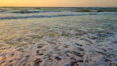 Fırtınalı deniz. Gün batımında ve şafakta denizde beyaz köpüklü büyük dalgalar. Mavi deniz, turuncu kırmızı gökyüzü, güneş. Sahil kıyısı kıyı şeridi. Doğal zemin arkaplan fırtınası Yavaş çekim