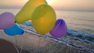 Şafak ve günbatımında denizin arka planında bir sürü renkli şişme top var. Gün batımında deniz kenarında elinde çok renkli hava balonlarıyla oynayan kişi. Eğlence, eğlence, mutlu sanat fikri, neşeli.