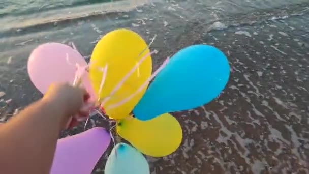 夜明けと日没に海の背景にある多くのカラフルな膨脹可能なボール 海岸の砂浜の海の波の背景に手元に多彩な風船で遊んでいる人 エンターテインメントの楽しみ — ストック動画