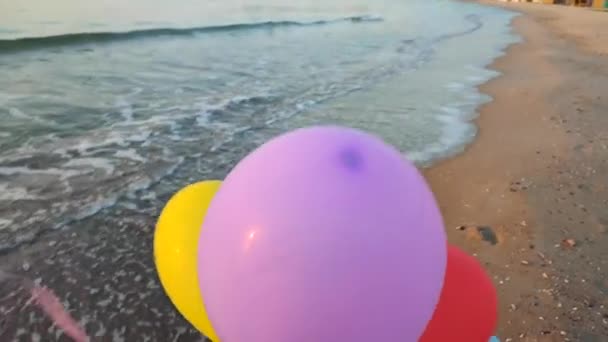夜明けと日没に海の背景にある多くのカラフルな膨脹可能なボール 海岸の砂浜の海の波の背景に手元に多彩な風船で遊んでいる人 エンターテインメントの楽しみ — ストック動画