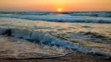 Fırtınalı deniz. Gün batımında ve şafakta denizde beyaz köpüklü büyük dalgalar. Mavi deniz, turuncu kırmızı gökyüzü ve güneş. Sahil kıyısı kıyı şeridi. Doğal arka plan doğa fırtınası