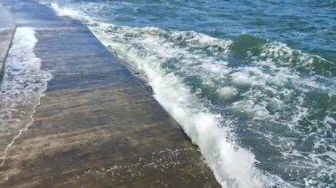 Fırtınalı deniz. Büyük deniz dalgaları güneşli yaz gününde eski beton iskeleye çarpıp çarpıyor. Beyaz köpüklü yüksek dalgalar. Büyük dalgalar kopuyor, çimento iskelesine yayılıyor. Patlamalar ve sıçramalar.