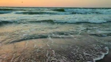 Fırtınalı deniz. Gün batımında ve şafakta denizde beyaz köpüklü büyük dalgalar. Mavi deniz, turuncu kırmızı gökyüzü ve güneş. Sahil kıyısı kıyı şeridi. Doğal arka plan doğa fırtınası