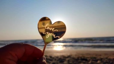 Elinde kalp şeklinde sarı yansıtıcı çubuk tutan kadın güneşli bir sabahta kumlu sahil sahilinde parlayan güneşin arka planında seni seviyor. Romantik Sevgililer Günü 'nü severim.
