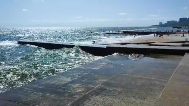 Fırtınalı deniz. Büyük deniz dalgaları güneşli yaz gününde eski beton iskeleye çarpıp çarpıyor. Beyaz köpüklü yüksek dalgalar. Büyük dalgalar kopuyor, çimento iskelesine yayılıyor. Patlamalar ve sıçramalar.