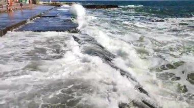 Fırtınalı deniz. Büyük deniz dalgaları güneşli yaz gününde eski beton iskeleye çarpıp çarpıyor. Beyaz köpüklü yüksek dalgalar. Büyük dalgalar kopuyor, çimento iskelesine yayılıyor. Patlamalar ve sıçramalar.