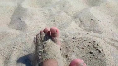 Ayakları kumda kazı yapan bir kadın. Sıcak yaz gününde kumsalda ayaklarını kuru kuma gömme oyunu oynayan biri. Tatil tatili, tatil, dinlenme, turizm...