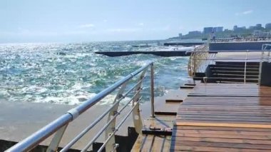Büyük dalgalar, güneşli bir günde bir sürü sıçramayla ahşap iskeleye çarpıyor. Fırtına, fırtınalı deniz. Hava durumu. Seyahat, turizm, tatil. Sahil, sahil, sahil