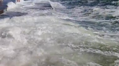 Büyük dalgalar eski çimento kıyısına çarpıyor. Güneşli bir günde dalgalar iskele iskelesine vuruyor. Fırtına, fırtınalı deniz. Hava durumu. Beyaz köpüklü yüksek dalgalar.