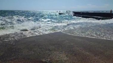 Güneşli bir günde eski çimento kıyısına büyük bir dalga düştü. Güneşli bir günde dalgalar iskele iskelesine vuruyor. Fırtına, fırtınalı deniz. Hava durumu. Beyaz köpüklü yüksek dalgalar.