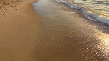Deniz dalgaları, güneşli bir şafak vakti kumlu sahil sahilinde dalgalanır. Köpüklü deniz dalgaları ve kıyıdaki kumlara sıçramalar. Sahil Kıyısı Sahili. Doğal arka plan. Doğa zemin.