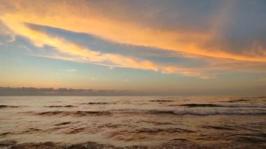 Denizde gün batımında gün doğumu. Şafağın kırmızı ışığı mavi gökyüzündeki bulutlar ve deniz suyunun yüzeyi tarafından yansıtılır. Dalgalar deniz kıyısının kumlu sahillerine vuruyor. Doğal arkaplan Doğa arkaplanı