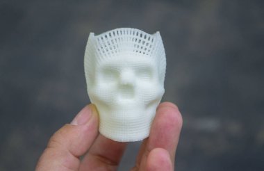 Elinde erimiş beyaz plastikten yapılmış insan kafatasının küçük prototipini tutan kişi. Üç boyutlu model. Katkı sağlayan ilerici tıbbi teknoloji. Modern yeni baskı endüstrisi.
