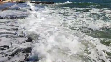 Büyük dalgalar eski çimento kıyısına çarpıyor. Güneşli bir günde dalgalar iskele iskelesine vuruyor. Fırtına, fırtınalı deniz. Hava durumu. Beyaz köpüklü yüksek dalgalar.