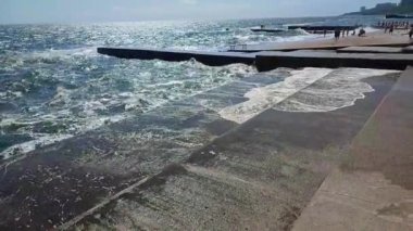 Fırtınalı deniz. Büyük deniz dalgaları güneşli yaz gününde eski beton iskeleye çarpıp çarpıyor. Beyaz köpüklü yüksek dalgalar. Büyük dalgalar kopuyor, çimento iskelesine yayılıyor. Patlamalar ve sıçramalar.