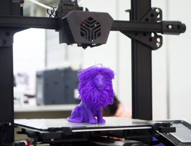 Model of toy lion printed on 3D printer from melted plastic blue color on desktop of 3D printer. Concept 3D printer, 3D printing, modeling prototyping three dimensional object. Innovative production clipart