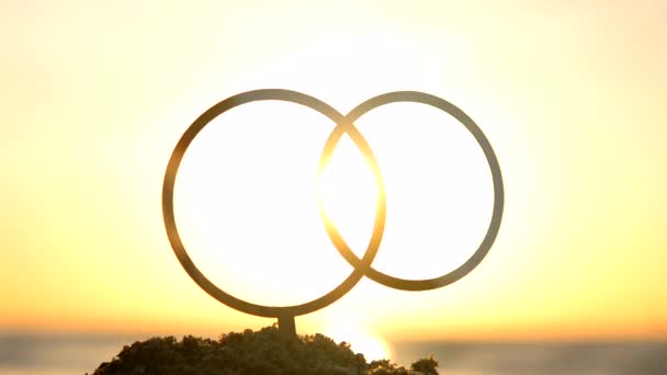 黄色い空の夜明けと日没に結婚指輪のブラックアウトライン セッティングと昇る太陽の背景に砂の結婚指輪の形をした輪郭をスティックします コンセプト 結婚式 ロマンチック バレンタインデー — ストック動画