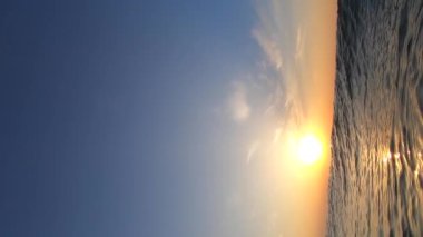 Deniz ve güneş. Dalgalanan dalgalar ve güneşli yollarla deniz suyu yüzeyi. Şafakta ve gün batımında parlayan güneş. Mavi gökyüzü ve beyaz tüy bulutları. Açık gökyüzü denizi. Alt açı. Yuvarlanan dalga. Su altı Görünümü Dikey