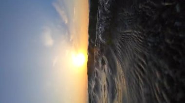 Deniz ve güneş. Dalgalanan dalgalar ve güneşli yollarla deniz suyu yüzeyi. Şafakta ve gün batımında parlayan güneş. Mavi gökyüzü ve beyaz tüy bulutları. Açık gökyüzü denizi. Alt açı. Yuvarlanan dalga. Su altı Görünümü Dikey