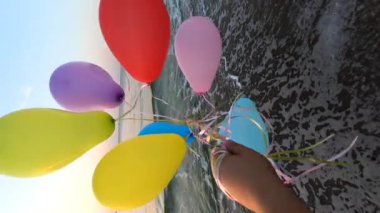 Deniz dalgaları yakınlarındaki kumlu sahil sahilinde bir sürü renkli balonla oynayan kişi. Çok renkli küçük balonlar elinde kurdeleyle kumun üzerine bağlanmıştı. Dinlenme eğlencesi şımartma Eğlence Dikey