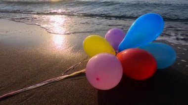 Güneşli bir sabah ve akşam deniz dalgalarıyla deniz kıyısındaki kumsalda uzanan bir sürü renkli balon. Eğlence eğlencesi, dinlenme, eğlence, bayram kutlaması. Yavaş çekim