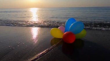 Güneşli bir sabah ve akşam deniz dalgalarıyla deniz kıyısındaki kumsalda uzanan bir sürü renkli balon. Eğlence eğlencesi, dinlenme, eğlence, bayram kutlaması. Yavaş çekim