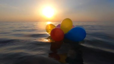 Güneşli bir yaz gününde bir grup renkli balon denizin dalgalarında salınır. Birçok renkli küçük balonlar birbirine bağlanmış olarak sabah gün batımında denizin yüzeyinde yüzerler.