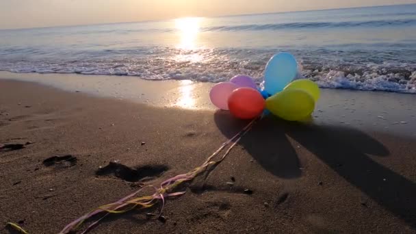 晴れた朝と夕方に海の波と海岸ビーチの砂の上に横たわる多彩な風船の打ち上げ レジャーエンターテイメントレクリエーション休憩楽しいお祝いの休日 スローモーション — ストック動画