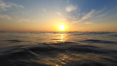 Deniz ve güneş. Dalgalanan dalgalar ve güneşli yollarla deniz suyu yüzeyi. Şafakta ve gün batımında parlayan güneş. Mavi gökyüzü ve beyaz tüy bulutları. Açık gökyüzü denizi. Alt açı. Doğal arka plan. Yavaş çekim