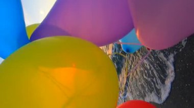 Gün doğumunda ve günbatımında deniz kıyısının kumlu sahilinde bir sürü renkli balonla oynayan bir kadın. Güneş balonların arasından parlıyor. Rahatla ve eğlen. Yavaş çekim Dikey