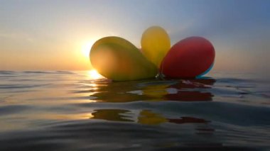 Güneşli bir yaz gününde bir grup renkli balon denizin dalgalarında salınır. Birçok renkli küçük balonlar birbirine bağlanmış olarak sabah gün batımında denizin yüzeyinde yüzerler.