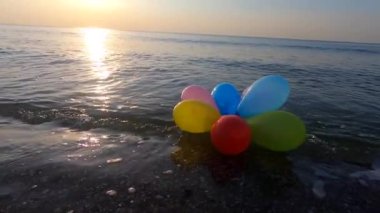 Güneşli bir sabah ve akşam deniz dalgalarıyla deniz kıyısındaki kumsalda uzanan bir sürü renkli balon. Eğlence eğlencesi, dinlenme, eğlence, bayram kutlaması. Yavaş çekim