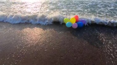 Güneşli bir sabah ve akşam deniz dalgalarıyla deniz kıyısındaki kumsalda uzanan bir sürü renkli balon. Eğlence eğlencesi, dinlenme, eğlence, bayram kutlaması. Yavaş çekim